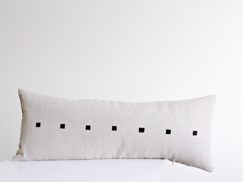 May include: A long, rectangular beige linen pillow with a row of black squares down the center.