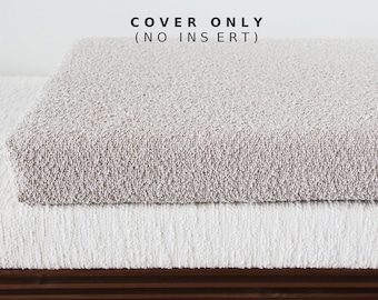 May include: A rectangular beige textured cushion cover with a thick, looped pile fabric. The text COVER ONLY (NO INSERT) is printed in black above the cushion. The cover rests on a white, vertically ribbed fabric surface with a dark wood base.
