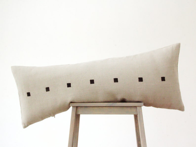 May include: A long, beige linen pillow with a row of black squares down the center.