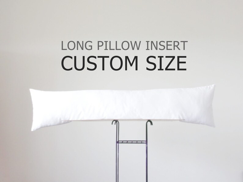 K&ouml;nnte beinhalten: Ein langes, wei&szlig;es Kissen, das auf einem schwarzen Metallst&auml;nder pr&auml;sentiert wird. Das Kissen ist rechteckig und scheint mit einem weichen Material gef&uuml;llt zu sein. &Uuml;ber dem Kissen steht der Text "LONG PILLOW INSERT CUSTOM SIZE."