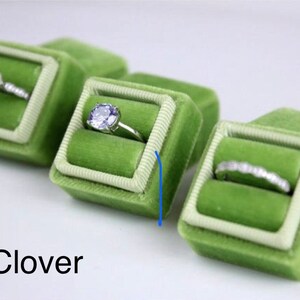 May include: Several green velvet ring boxes with white trim, each holding a different engagement ring. The rings feature various diamond cuts and settings. The word "Clover" is printed in black at the bottom of the image.