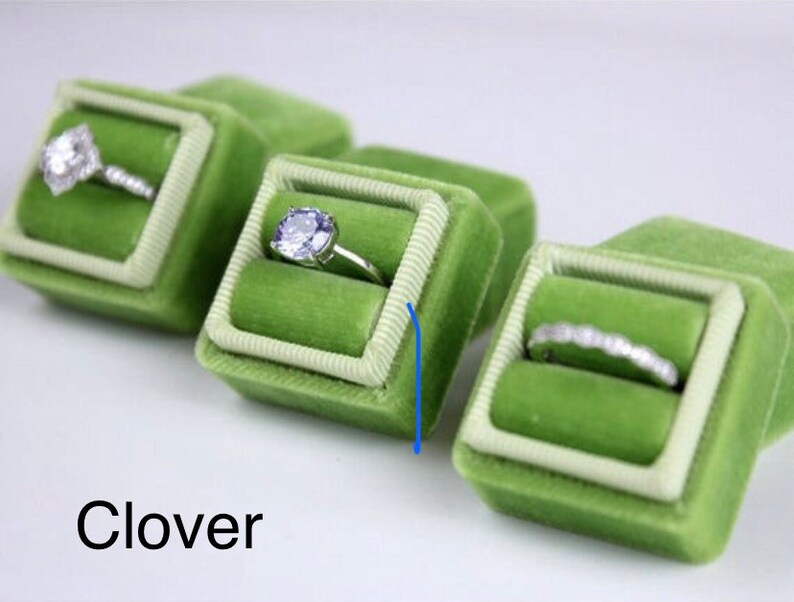 May include: Several green velvet ring boxes with white trim, each holding a different engagement ring. The rings feature various diamond cuts and settings. The word "Clover" is printed in black at the bottom of the image.