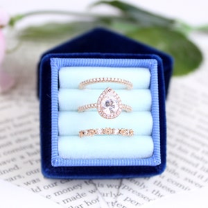 Könnte beinhalten: Drei goldene Ringe mit Diamanten werden in einer blauen Samt-Ringbox mit hellblauem Innenraum präsentiert. Die Ringe sind übereinander gestapelt.