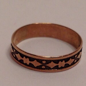May include: A gold band ring with a black geometric design. The ring is simple and elegant.