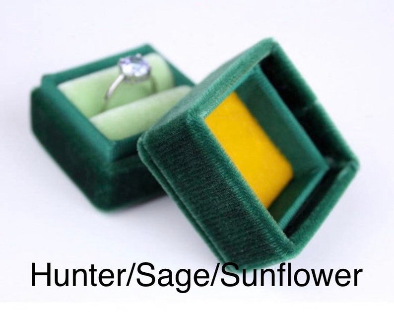 May include: A dark green velvet ring box with a light green interior and a yellow base. A silver ring with a light blue gemstone sits inside the open box. The text "Hunter/Sage/Sunflower" is at the bottom.