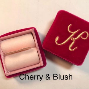 May include: Open cherry red velvet ring box with a blush pink interior. The lid of the box is embroidered with a gold letter "K". The text "Cherry & Blush" is at the bottom of the image.