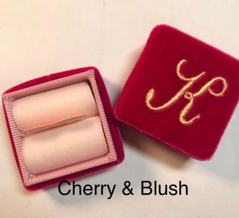 May include: Open cherry red velvet ring box with a blush pink interior. The lid of the box is embroidered with a gold letter "K". The text "Cherry & Blush" is at the bottom of the image.
