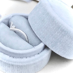 May include: A silver ring with a single diamond set in a V-shaped design, displayed in a light blue velvet ring box.
