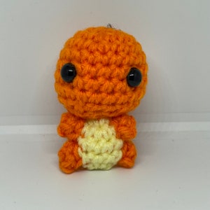 May include: Orange and yellow crocheted plush toy with black eyes. The toy is shaped like a small creature with a round head and a small body.