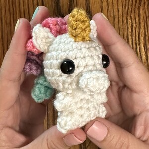 May include: A white crocheted unicorn with a gold horn, pink, purple, and green yarn mane, and black eyes.