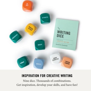 May include: Nine wooden dice with various words printed on each side, including "Uneducated", "Woman", "Vs. Self", "Medieval History", "Optimistic", "Greedy", "Identity", "Minor Character", and "Foreign Country". The dice are arranged on a white surface with a green card that reads "Writing Dice: Inspiration for Creative Writing. Banish the blank page."
