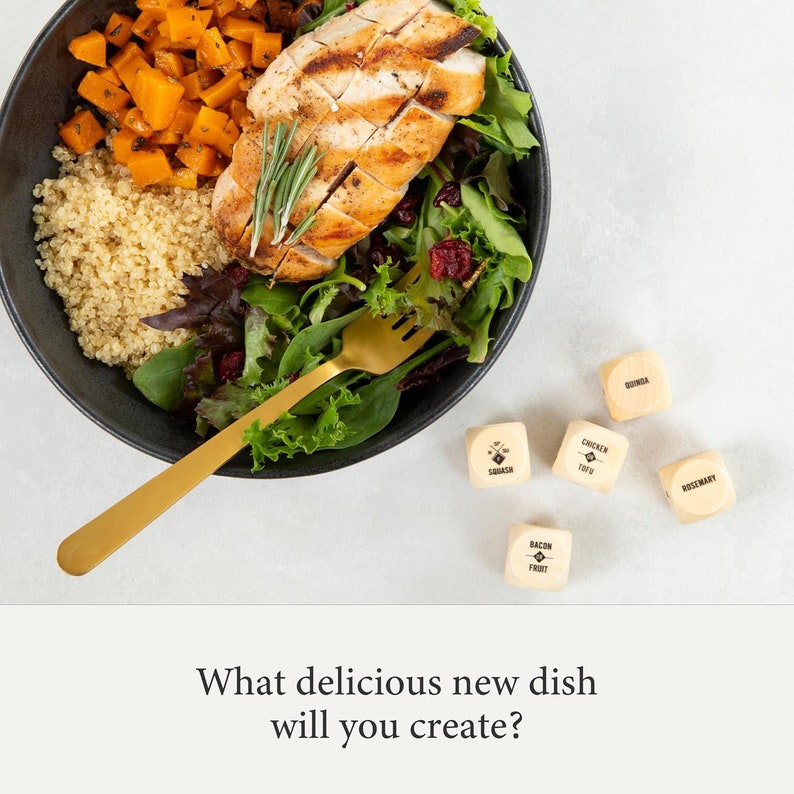 May include: A black bowl filled with a salad with quinoa, butternut squash, greens, and grilled chicken.  A gold fork is in the bowl.  Five wooden dice with different food ingredients are scattered on a white surface.  The dice read: Quinoa, Chicken Tofu, Rosemary, Bacon Fruit, and Squash.