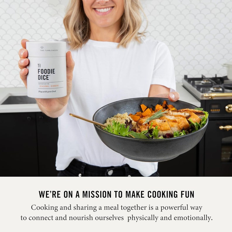 May include: A white cylinder container with the text "YP FOODIE DICE" and "Inspiration for Seasonal Eating" printed on it. The container is being held by a person in front of a bowl of food.
