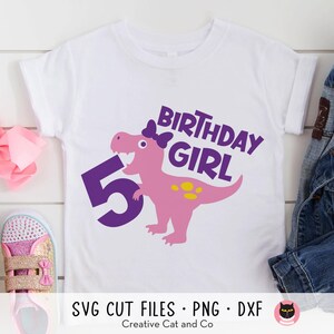 K&ouml;nnte beinhalten: Wei&szlig;es T-Shirt mit einer lila Zahl 5, einem rosa Dinosaurier mit einer lila Schleife und dem Text "Birthday Girl" in lila.