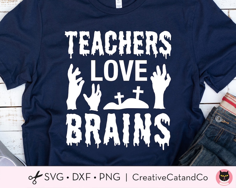 K&ouml;nnte beinhalten: Ein dunkelblaues T-Shirt mit einem wei&szlig;en Grafikdesign, auf dem "Teachers Love Brains" mit Zombie-H&auml;nden und einem Friedhof steht.