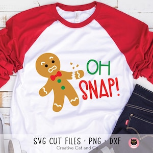 May include: A white and red baseball tee shirt with a gingerbread man with a broken arm and the text "OH SNAP!" printed on the front.