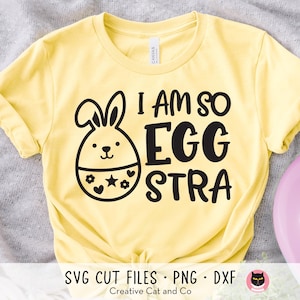 May include: A yellow t-shirt with the phrase "I AM SO EGG STRA" in black lettering. A cartoon bunny with a floral and star design is on the left. The shirt also has the text "SVG CUT FILES • PNG • DXF" and "Creative Cat and Co."