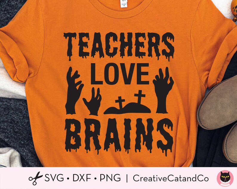 K&ouml;nnte beinhalten: Orangefarbenes T-Shirt mit schwarzem Text, der "Teachers Love Brains" mit einem Tropfeffekt lautet. Der Text ist von schwarzen Zombie-Handsilhouetten und einem kleinen Friedhof mit zwei Kreuzen umgeben.