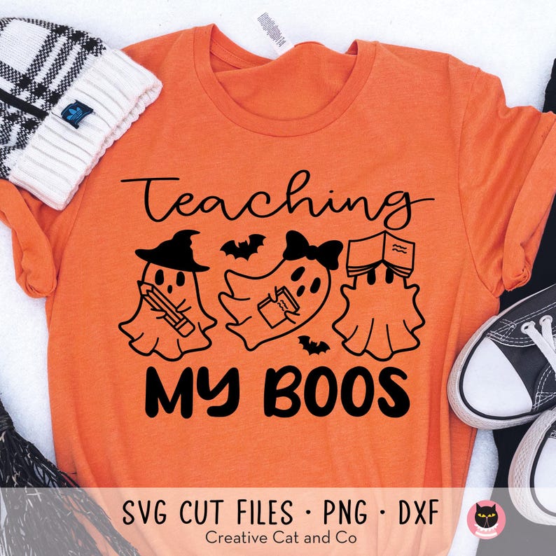 May include: Orange t-shirt with black text that reads "Teaching My Boos". The text is surrounded by three ghosts, one holding a book, one holding a pencil, and one holding a book. The ghosts are all wearing witch hats or bows.