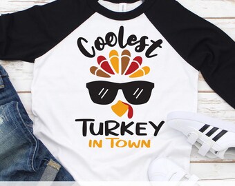 May include: White raglan t-shirt with black sleeves featuring a turkey wearing sunglasses and the text "Coolest Turkey in Town".