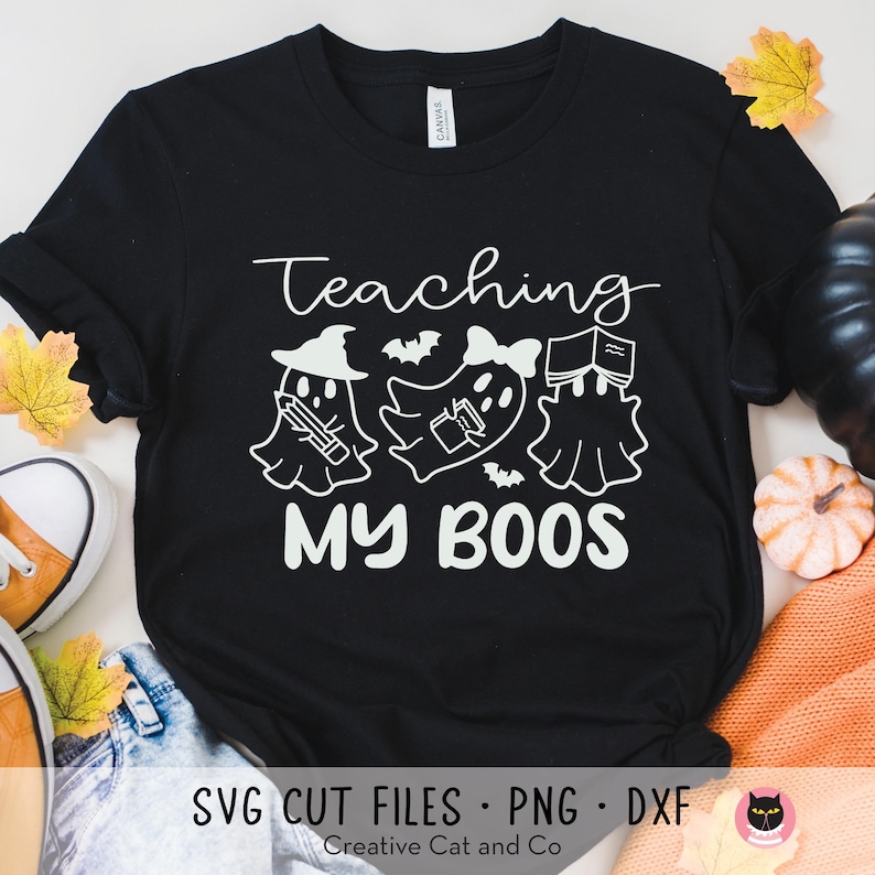 May include: Black t-shirt with white text that reads "Teaching My Boo's". The text is surrounded by three ghosts holding books and pencils.