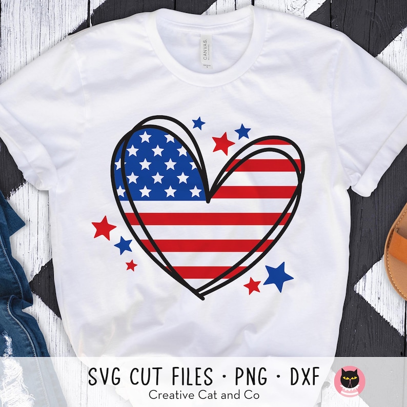 May include: White t-shirt with a red, white, and blue heart-shaped American flag design. The heart is outlined in black and surrounded by small red and blue stars. The text "SVG CUT FILES - PNG - DXF" is at the bottom of the shirt. The text "Creative Cat and Co" is below the text "SVG CUT FILES - PNG - DXF".