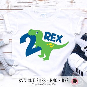 May include: White t-shirt with a green dinosaur holding a blue number 2 and the word "REX" in blue letters.