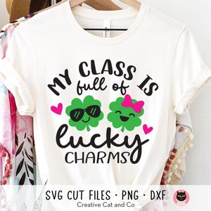 May include: White t-shirt with black text that reads "My class is full of lucky charms". The text is surrounded by two green shamrock graphics with smiling faces. One shamrock has sunglasses and the other has a pink bow.
