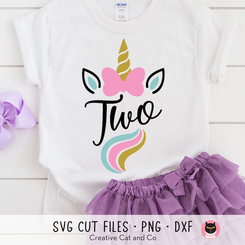 May include: White t-shirt with a unicorn design and the word "Two" in pink, blue, and gold. The unicorn has a pink bow and a gold horn.