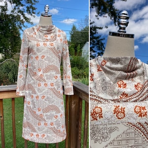 May include: A white dress with a brown and orange geometric pattern. The dress has a high neck and long sleeves.