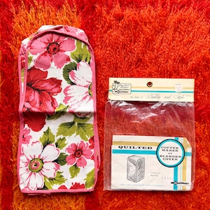 May include: A vintage floral oven mitt and a quilted coffee maker or blender cover. The oven mitt features large pink and red flowers with green leaves on a white background, trimmed with pink. The cover is in a plastic package with the text "Quality and Style".