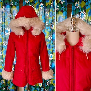 May include: A vibrant red winter coat with a hood and faux fur trim. The coat features a zipper closure, pockets, and fur cuffs. The hood and cuffs are trimmed with fluffy white faux fur. A vintage style winter coat.