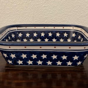 May include: Rectangular ceramic dish with a blue and white star pattern. The dish has a dark blue rim and a white interior. The exterior features a repeating pattern of white stars on a blue background. The dish is likely used for serving or baking.