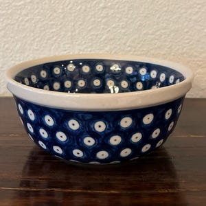 May include: A ceramic bowl featuring a deep blue glaze decorated with a repeating pattern of white circles with small dark centers. The bowl has a thick, smooth, cream-colored rim and a rounded body, showcasing a consistent hand-painted aesthetic.