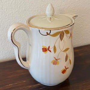 May include: A set of three ceramic mugs with a speckled, cream-colored glaze. Each mug features a different hand-painted design: a blue and green leaf, a yellow flower, and a red berry. The mugs have a simple, modern design.