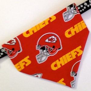 Puede incluir: Bandana roja para perro con un patr&oacute;n repetido de texto amarillo "Chiefs" y un casco de f&uacute;tbol blanco con un logotipo rojo y amarillo. El logotipo es una "K" estilizada con un "5" rojo en su interior.