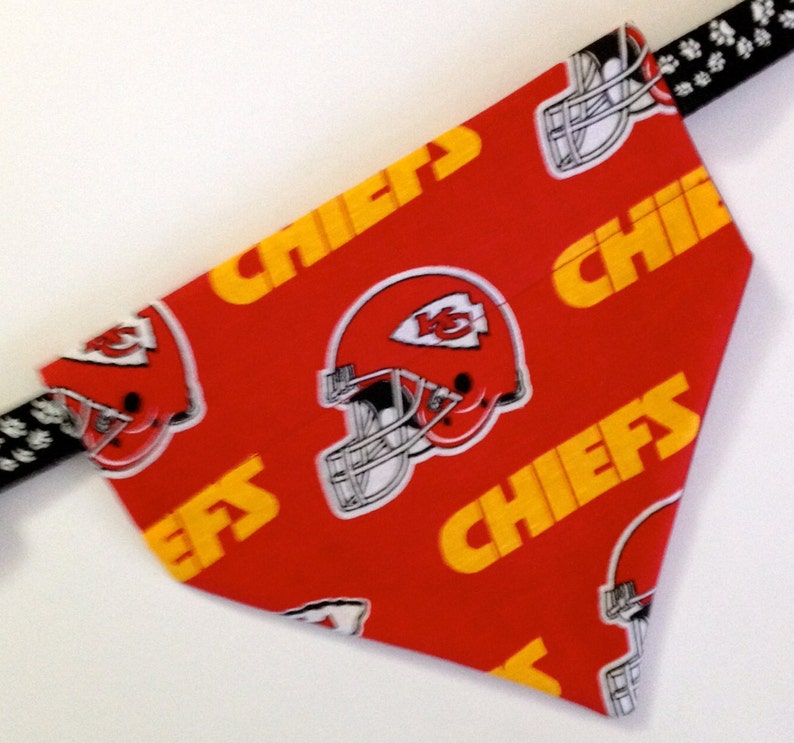 Puede incluir: Bandana roja para perro con un patr&oacute;n repetido de texto amarillo "Chiefs" y un casco de f&uacute;tbol blanco con un logotipo rojo y amarillo. El logotipo es una "K" estilizada con un "5" rojo en su interior.
