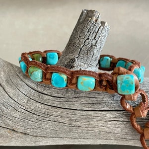 May include: A brown leather bracelet with turquoise stones. The bracelet is wrapped around a piece of driftwood.