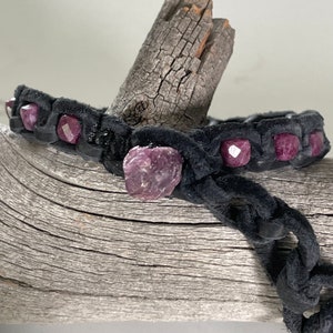 Op de afbeelding: Een zwarte leren armband met roze edelsteen kralen. De armband is gevlochten en heeft een knoopsluiting.