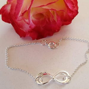 May include: A silver infinity symbol charm bracelet with a delicate chain. The bracelet has a lobster clasp closure.