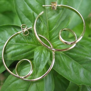 May include: A pair of gold hoop earrings with a unique twist design. The earrings are made of a single piece of wire that is twisted into a circle and then bent into a hoop shape.