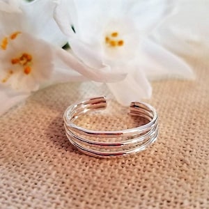 May include: A silver ring with four bands stacked on top of each other. The ring is made of smooth, polished metal.