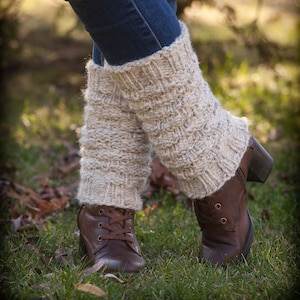 May include: A pair of beige knitted leg warmers worn over blue jeans and brown ankle boots.