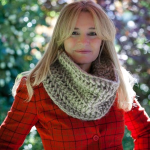 May include: A woman wearing a red and black plaid jacket with a gray knitted cowl neck scarf. The scarf is thick and chunky and has a loose, drapey style.