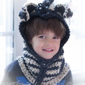 May include: A child wearing a black and white striped crocheted hat and scarf with a black button. The hat has a pointed top and the scarf is a cowl style.