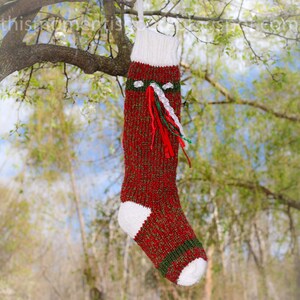 Peut inclure: Une chaussette de No&euml;l rouge et verte en tricot avec une bordure blanche et un pompon blanc sur le dessus. La chaussette est d&eacute;cor&eacute;e de rubans verts, blancs et rouges.