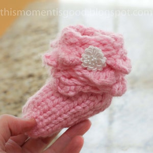 May include: Pink crocheted baby booties with a white flower embellishment.