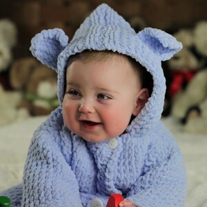 May include: A baby wearing a light blue hooded knitted sweater with bear ears. The baby is playing with a wooden toy with colorful pegs.