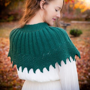 May include: A green knitted shawl with a scalloped edge. The shawl is draped over the shoulders of a person wearing a white dress.