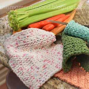 Puede incluir: Cuatro pa&ntilde;os de cocina de ganchillo en diferentes colores: blanco con motas rosas y azules, verde, azul claro y melocot&oacute;n. Los pa&ntilde;os de cocina est&aacute;n doblados y dispuestos sobre una encimera con apio y zanahorias en el fondo.